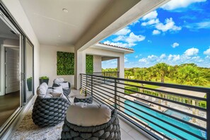 A balcony with a pool, outdoor seating, and a view of a lush landscape.