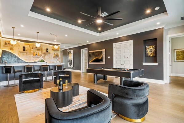 A modern living room with a pool table, comfortable seating, and a bar area.