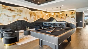 A modern pool table with a black and grey color scheme, surrounded by black cushioned seating and a decorative wall with a wavy pattern.
