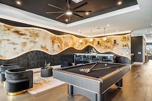 Una mesa de billar moderna con una paleta de colores negra y gris, rodeada de asientos acolchados negros y una pared decorativa con un diseño ondulado.