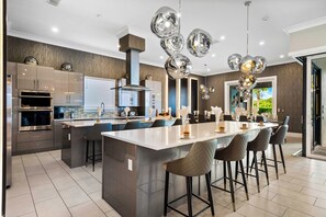 A modern kitchen with a central island, bar stools, and a dining area with a view of the outdoors.