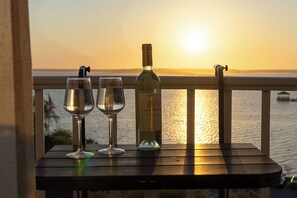 Ett bord med två vinglas och en vinflaska, placerat med utsikt över en solnedgång över vattnet.