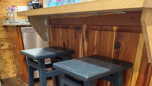 A kitchen area with wooden cabinets, a countertop, and two dark-colored stools. - Welcome to Jackson Hole A Charming 1-bedroom house in Historic Mineola. (Mineola)
