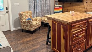 A modern kitchen with a wooden island, a ceiling fan, and a flat-screen TV mounted on a wooden wall. - Welcome to Jackson Hole A Charming 1-bedroom house in Historic Mineola. (Mineola)