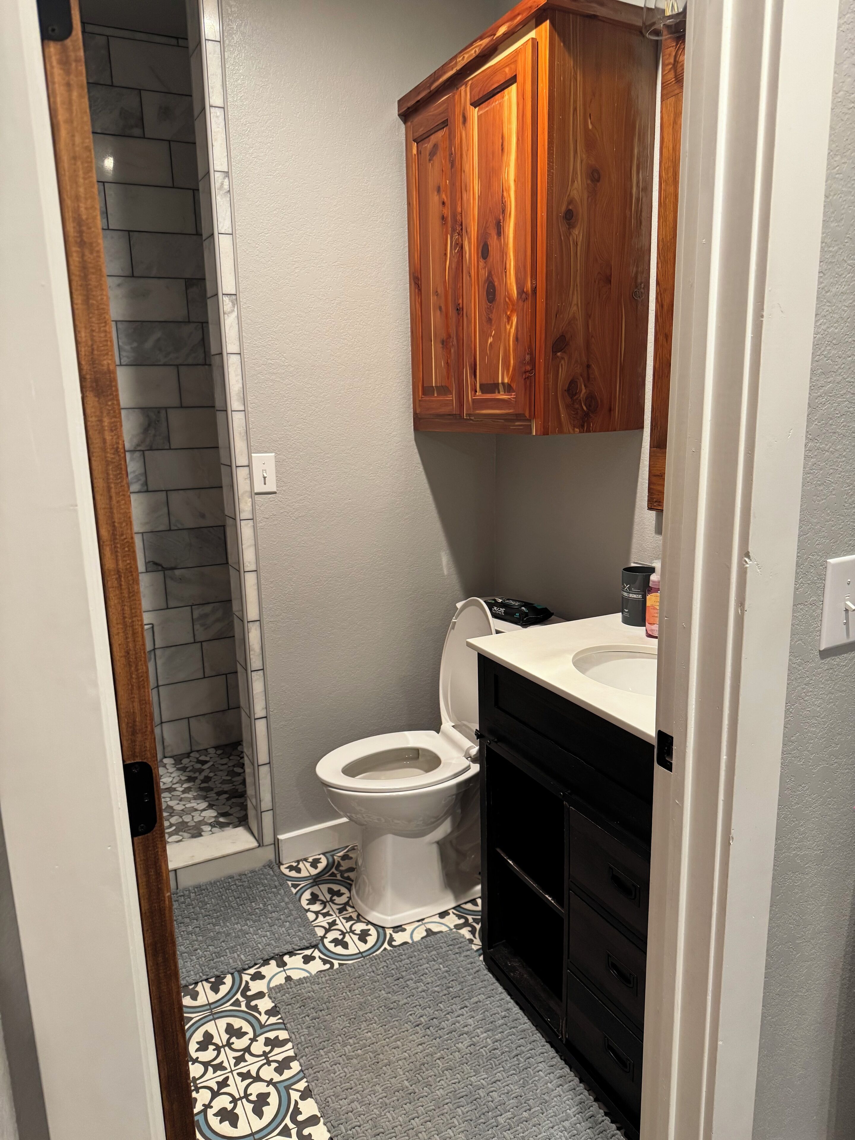 A bathroom with a toilet, wooden cabinets, a sink, and a shower area with a tiled floor.