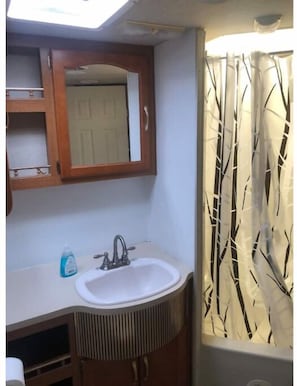 Bathroom features a sink, mirror, and cabinet with shelf, plus a window with a curtain.