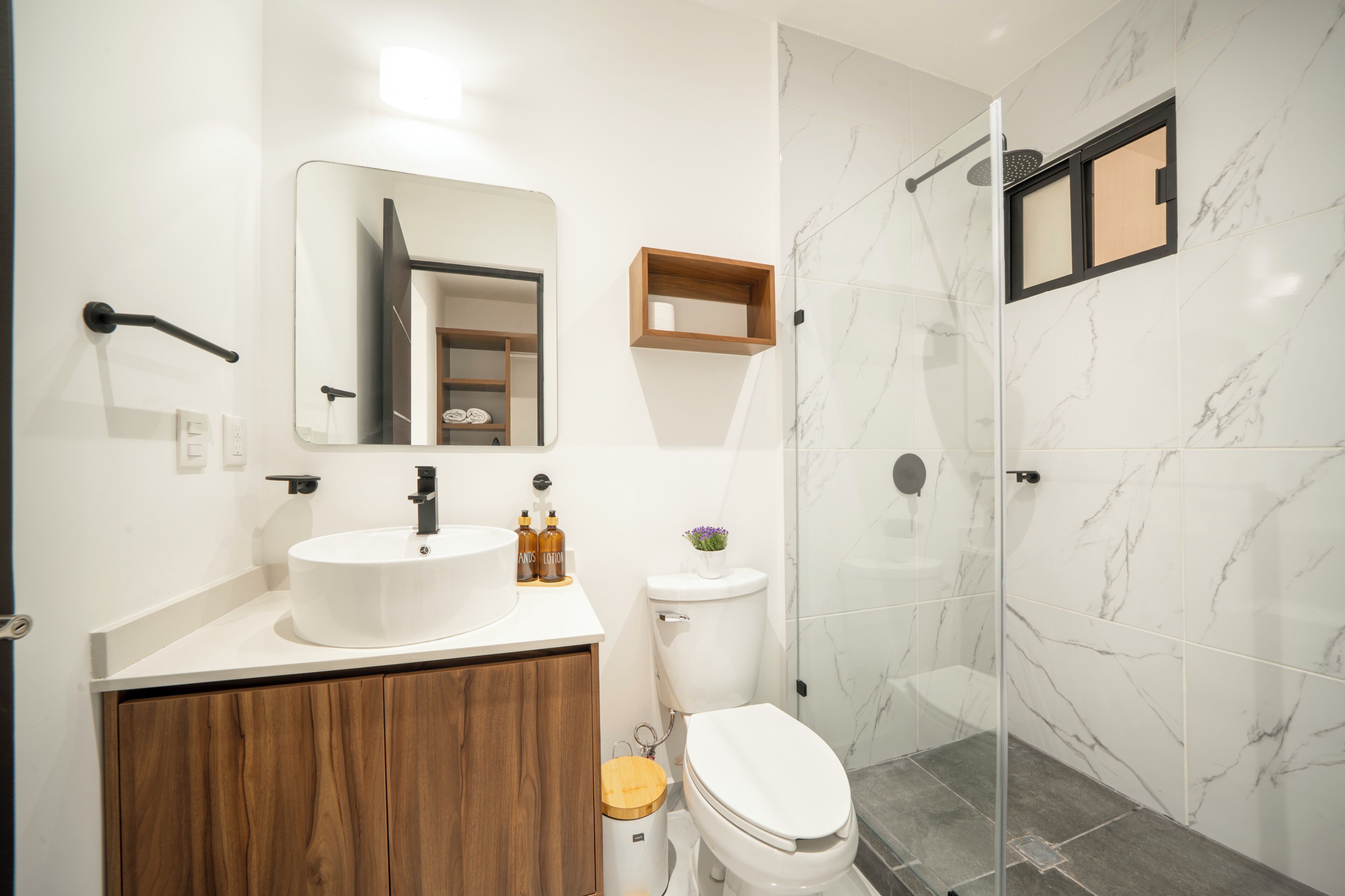 A modern bathroom with a white sink, wooden vanity, a toilet, and a glass-enclosed shower area.