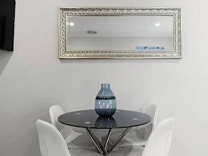 A round glass table with a blue vase, surrounded by white chairs, under a decorative mirror. - Prickly Pear Stays in Mayfield West (Mayfield West)