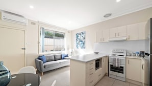 A compact kitchen with a built-in stove, a dining area with a table and chairs, and a gray sofa. - Prickly Pear Stays in Mayfield West (Mayfield West)