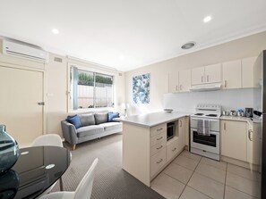 A compact kitchen with a built-in stove, a dining area with a table and chairs, and a gray sofa. - Prickly Pear Stays in Mayfield West (Mayfield West)