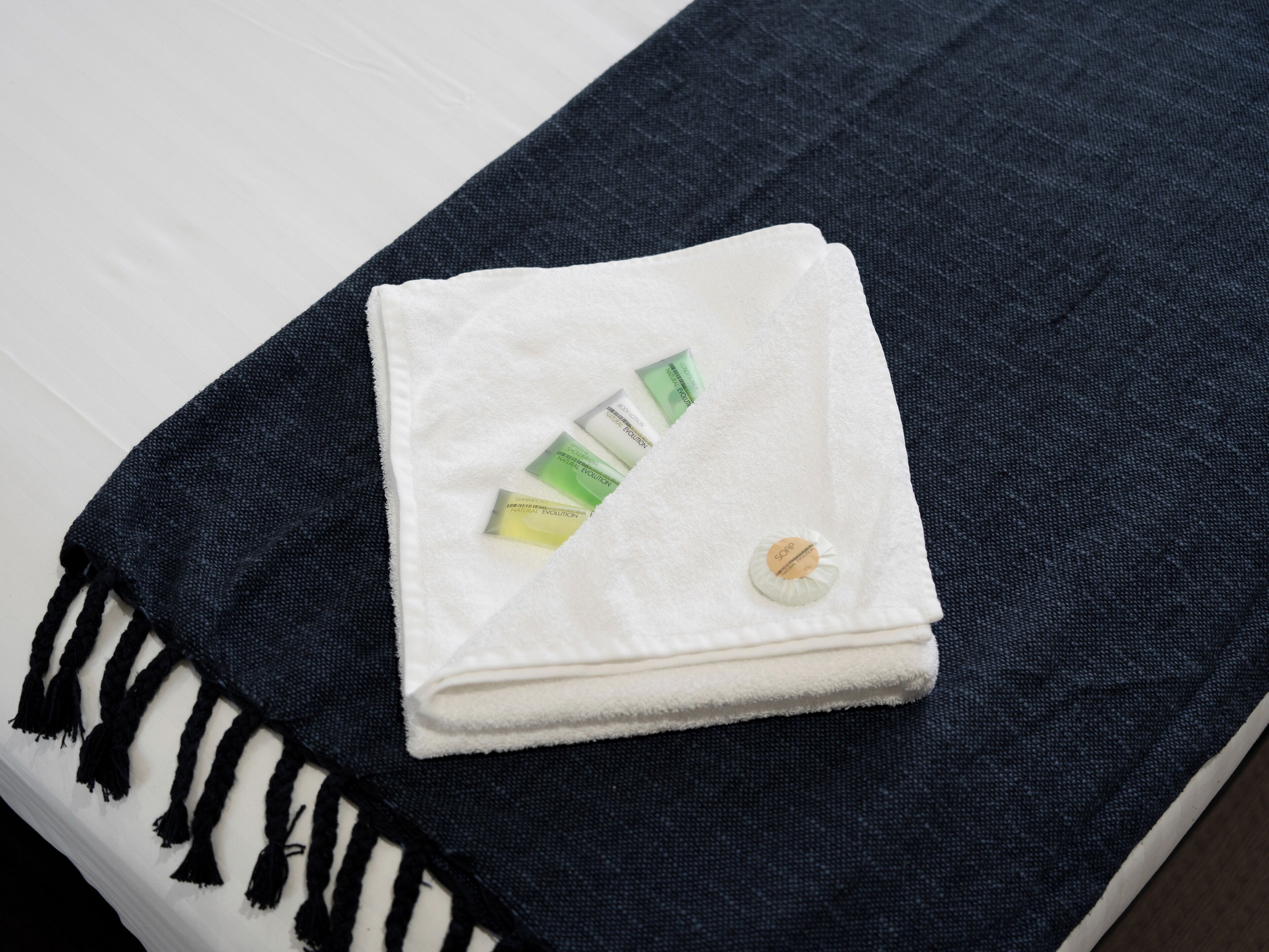 A neatly folded white towel with a small round tag on a dark blue towel on a bed.
