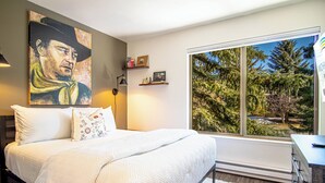 Een slaapkamer met een groot bed, een schilderij aan de muur en een raam met uitzicht op bomen.