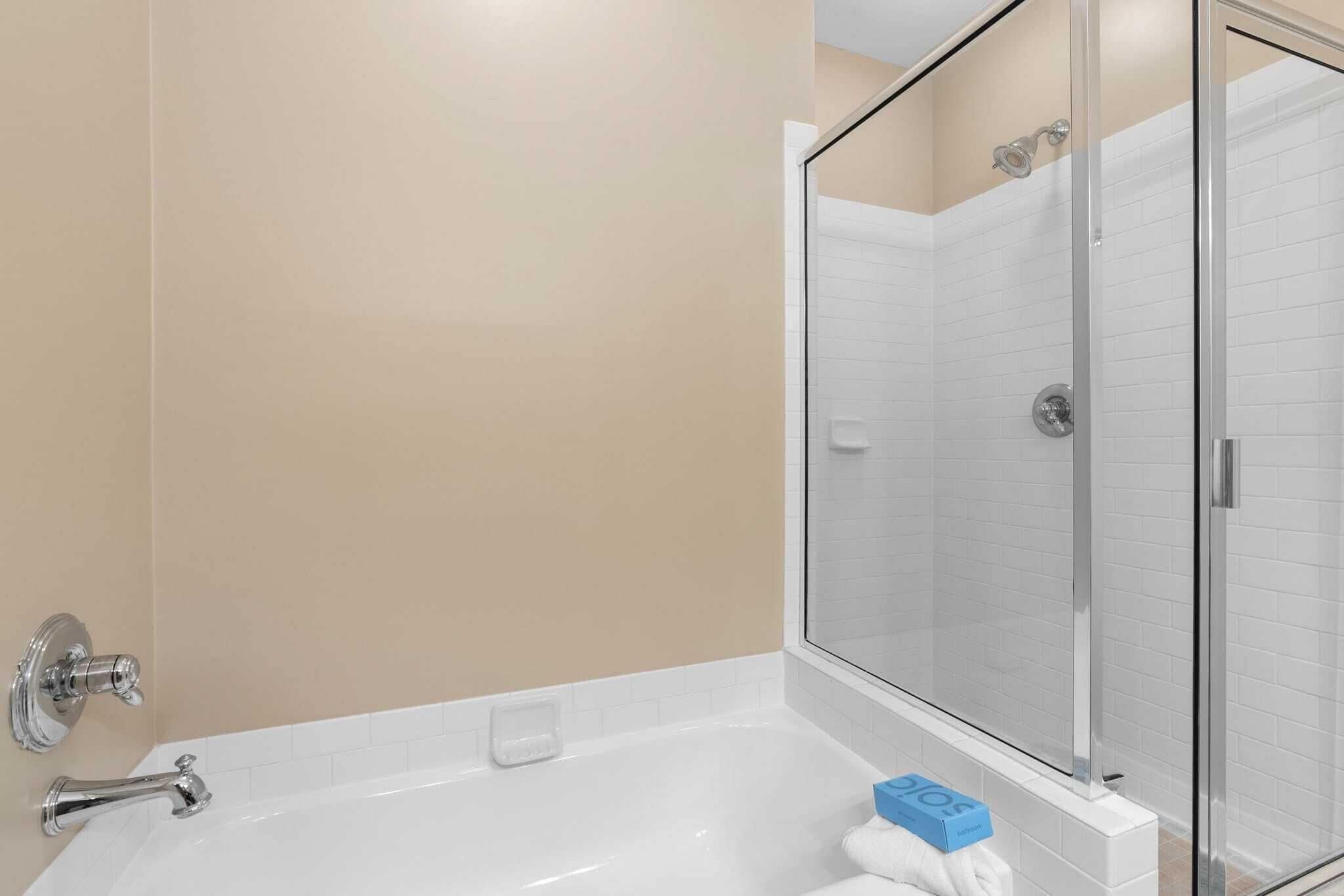 A modern bathroom with a bathtub, a glass shower enclosure, and a beige wall.