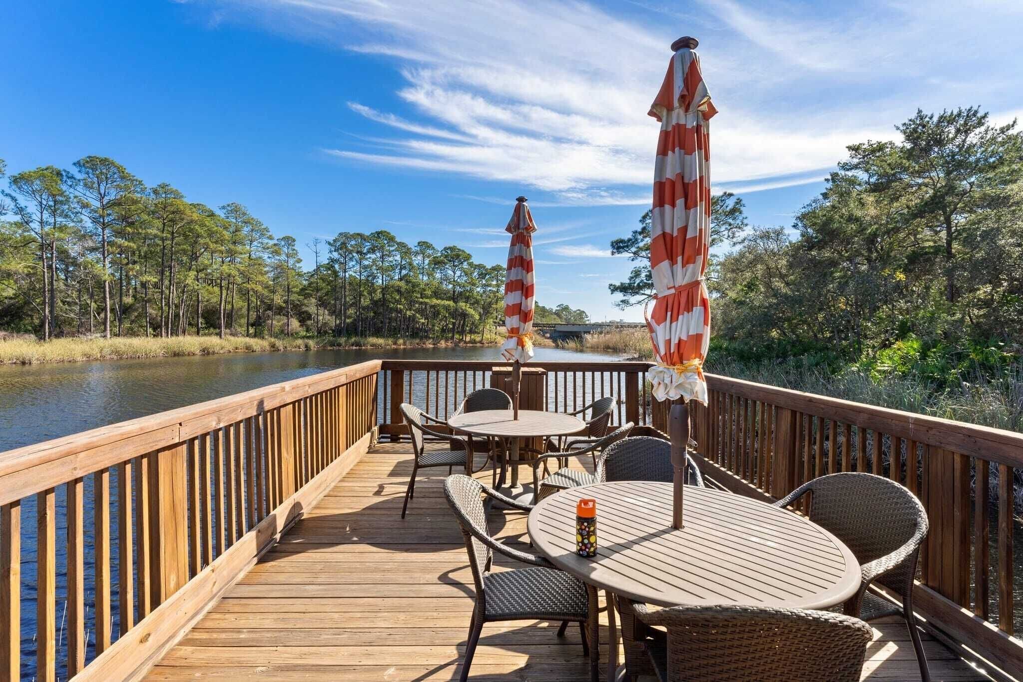 A wooden deck with outdoor furniture and striped umbrellas overlooking a body of water.