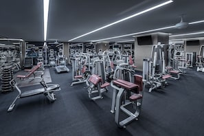 A gym with various exercise machines, mirrors, and a ceiling fan.