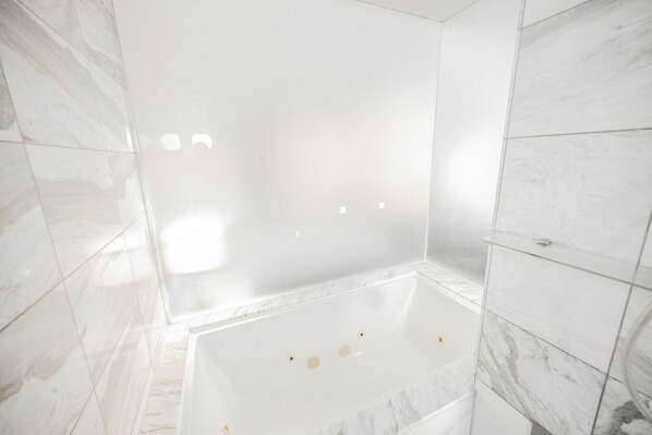 A modern bathroom with a large bathtub, marble tiles, and a shower area.