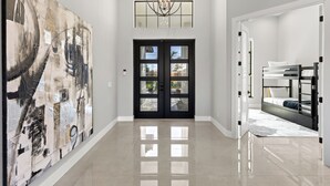A spacious hallway with a large abstract painting on the left, a black double door at the end, and a bunk bed in the right room.