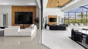 A spacious living area with a large flat-screen TV, modern furniture, and a balcony with outdoor seating.
