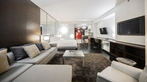 Een moderne hotelkamer met een bank, een klein bijzettafeltje, een televisie en een kitchenette.