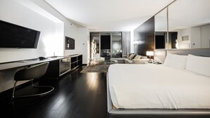 Een moderne hotelkamer met een groot bed, een bureau met een flatscreen-televisie, een bank en uitzicht op de stad.
