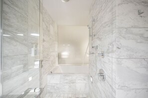 Un baño moderno con cabina de ducha de vidrio, paredes de mármol y un banco integrado.