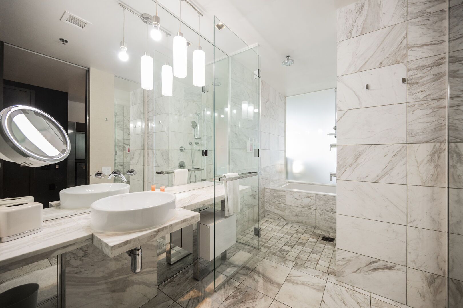 Un baño moderno con dos lavamanos, ducha con cerramiento de vidrio y suelo de mármol.