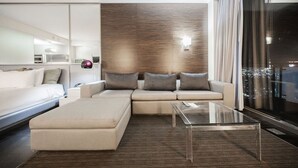 Een moderne woonkamer met een bank, een poef en een glazen salontafel.