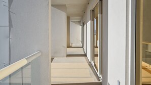 A corridor with a light-colored floor, white walls, and a glass door on the right.