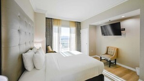 A hotel room with a large bed, a TV mounted on the wall, a chair, and a view through the window.