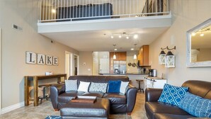 A spacious living room with a brown leather sofa set, a coffee table, and a patterned rug. A kitchen is visible in the background with modern appliances. - Family-Friendly, Fishing, & Fun w/ 2 Pools, Views, Boat Slip & Launch (Camdenton)