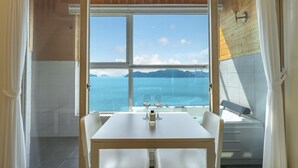 A dining area with a table and chairs, a view of the sea, and a bottle of perfume on the table. - Yeosu Jangsuri Poolvilla&spa Pension (Yeosu)