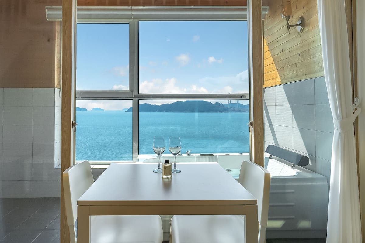 A dining area with a table and chairs, a view of the sea, and a bottle of perfume on the table.