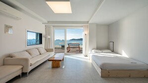 A modern hotel room with a large bed, a sofa, a wooden coffee table, and a view of the sea. - Yeosu Jangsuri Poolvilla&spa Pension (Yeosu)