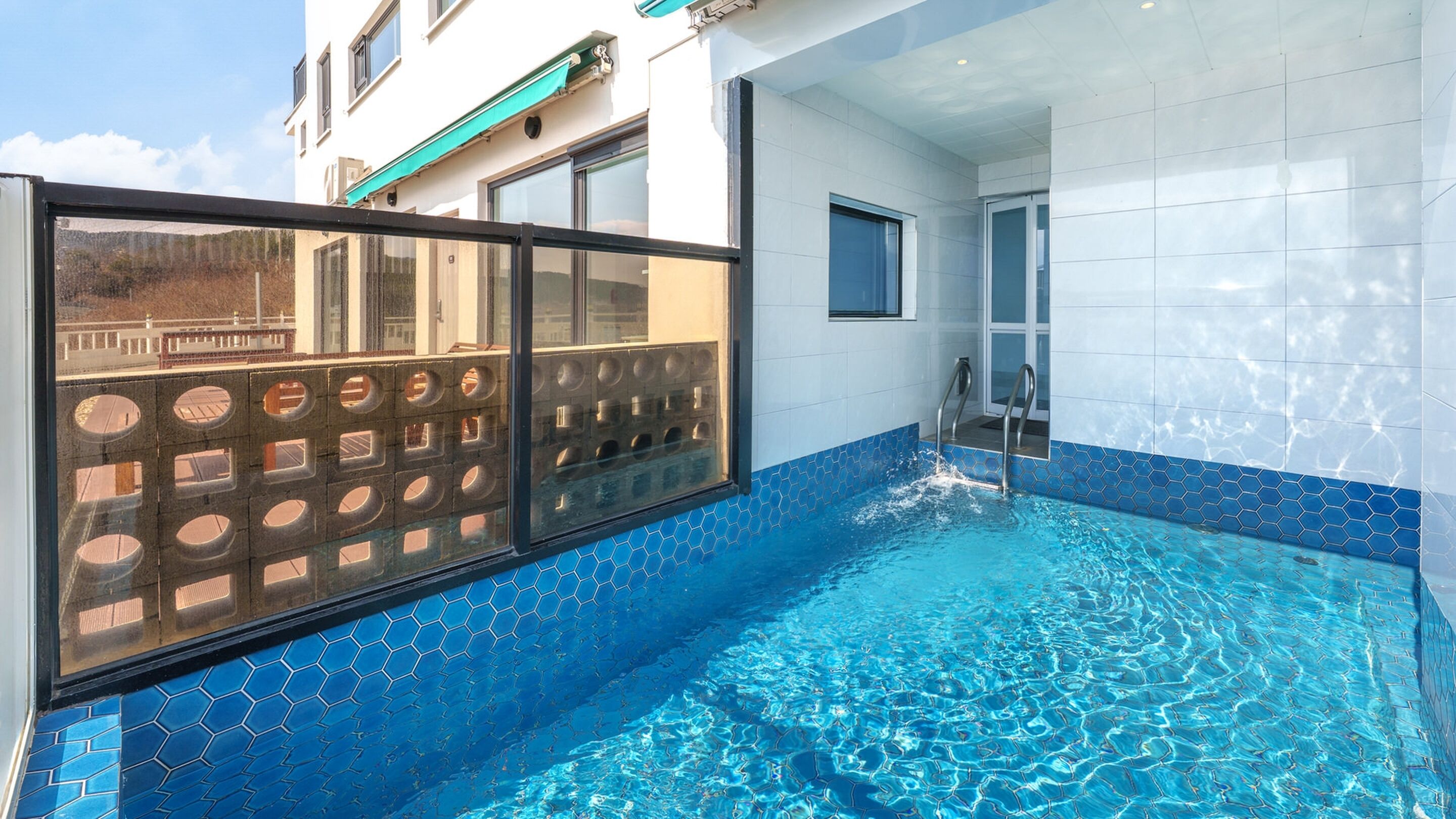 En swimmingpool med blå, sekskantede fliser, et glasindhegning og en metalstige.