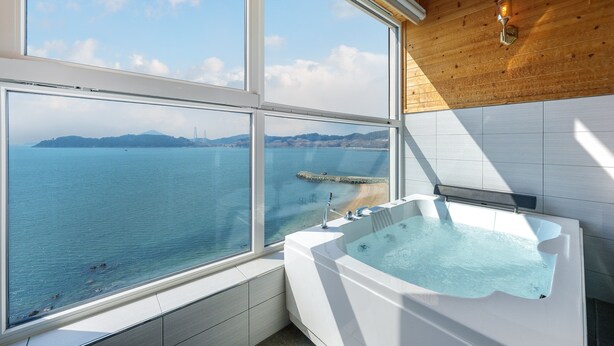 A bathroom with a large window overlooking a beach and sea, a bathtub, and wooden ceiling. - Yeosu Jangsuri Poolvilla&spa Pension (Yeosu)