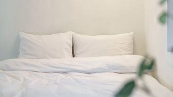 A neatly made bed with white linens in a room with plain walls.