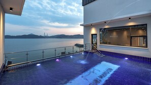 A modern building with a pool area, a view of the water, and a distant bridge. - Yeosu Jangsuri Poolvilla&spa Pension (Yeosu)