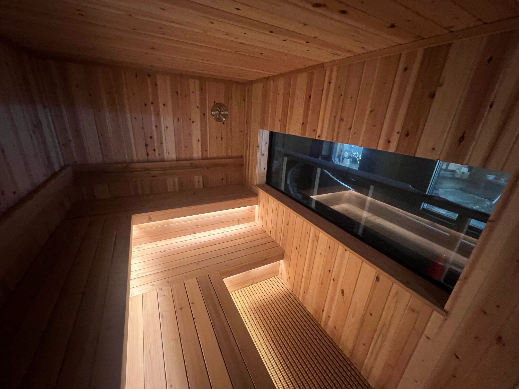 A sauna with wooden walls and a glass window.