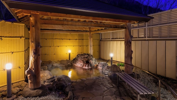 Un site de sources chaudes comprenant un pavillon en bois, des bancs en pierre et une petite cascade.