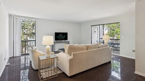 Een moderne woonkamer met een bank, een bijzettafeltje met een lamp en een flatscreen televisie op een meubel.