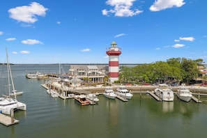 Een jachthaven met meerdere boten afgemeerd, een opvallend vuurtoren en een gebouw met een balkon dat uitzicht geeft op het water.