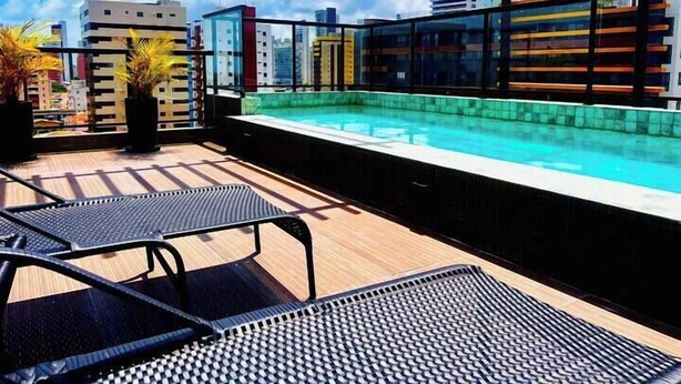 A rooftop pool with a clear view of the city skyline, two lounge chairs, and potted plants. - Solon Sales Luxor Prime (João Pessoa)