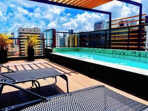 A rooftop pool with a clear view of the city skyline, two lounge chairs, and potted plants. - Solon Sales Luxor Prime (João Pessoa)