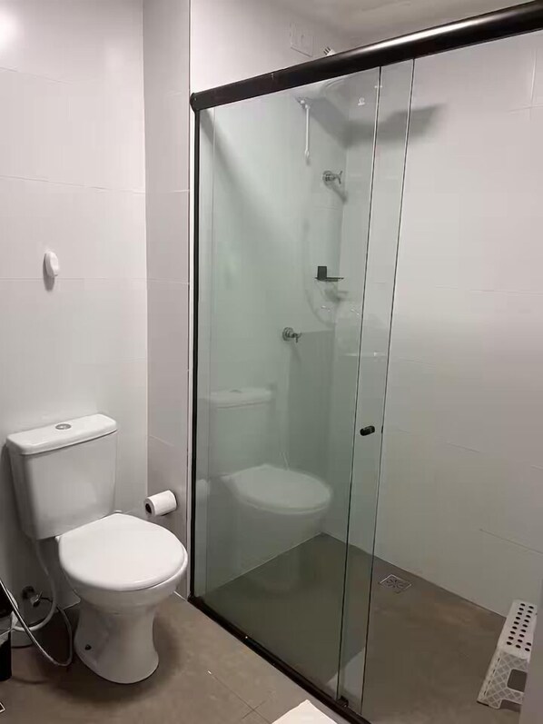 A modern bathroom with a glass-enclosed shower, a toilet, and a visible toilet paper roll.