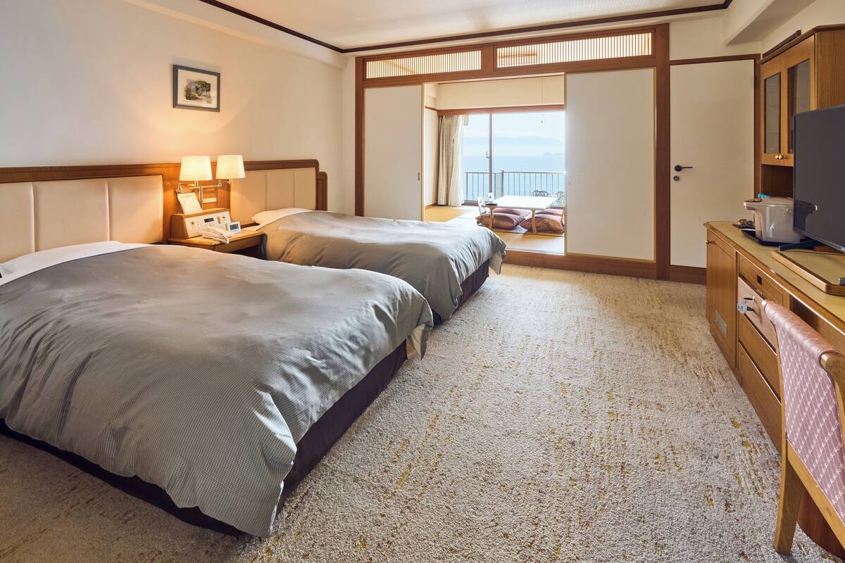 Une chambre d’hôtel avec deux lits, un bureau avec une télévision et un balcon avec vue.