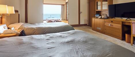 A hotel room with two beds, a desk with a TV, a minibar, and a view of the balcony.