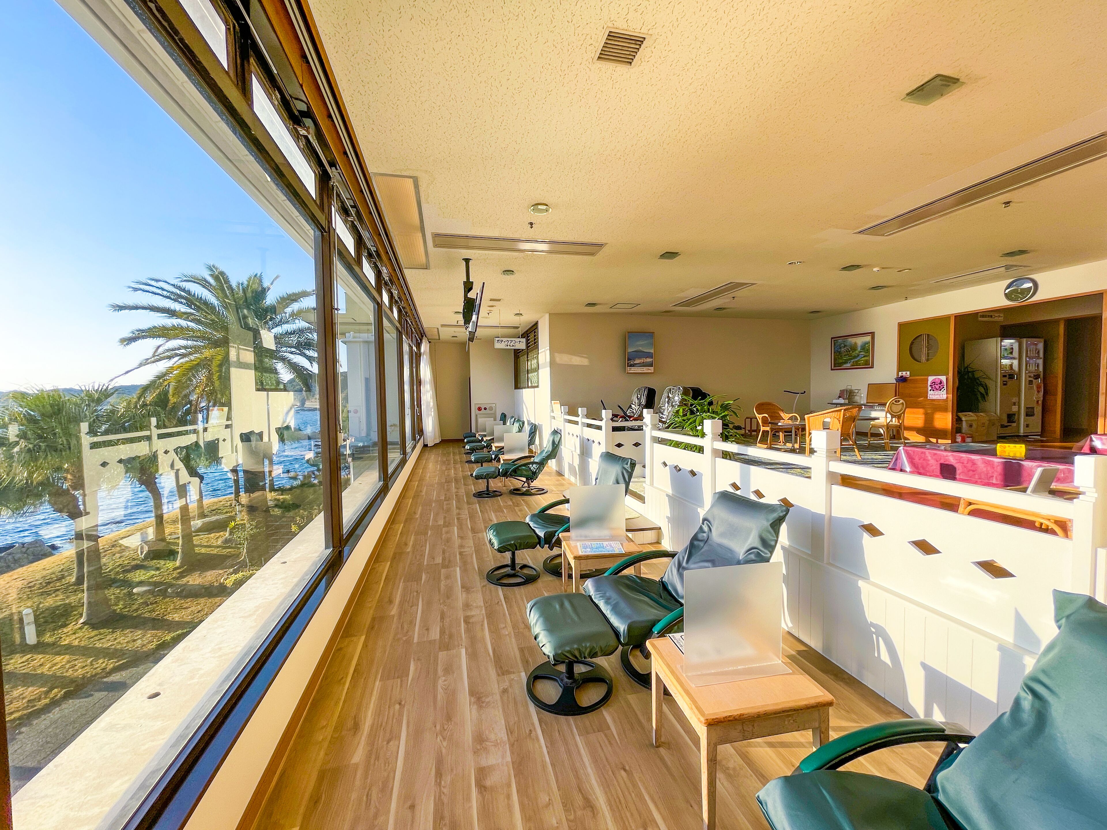 A hotel room with a large window overlooking a pool and palm trees, a wooden floor, and a seating area with chairs and a table.