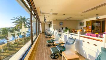 A hotel room with a large window overlooking a pool and palm trees, a wooden floor, and a seating area with chairs and a table.