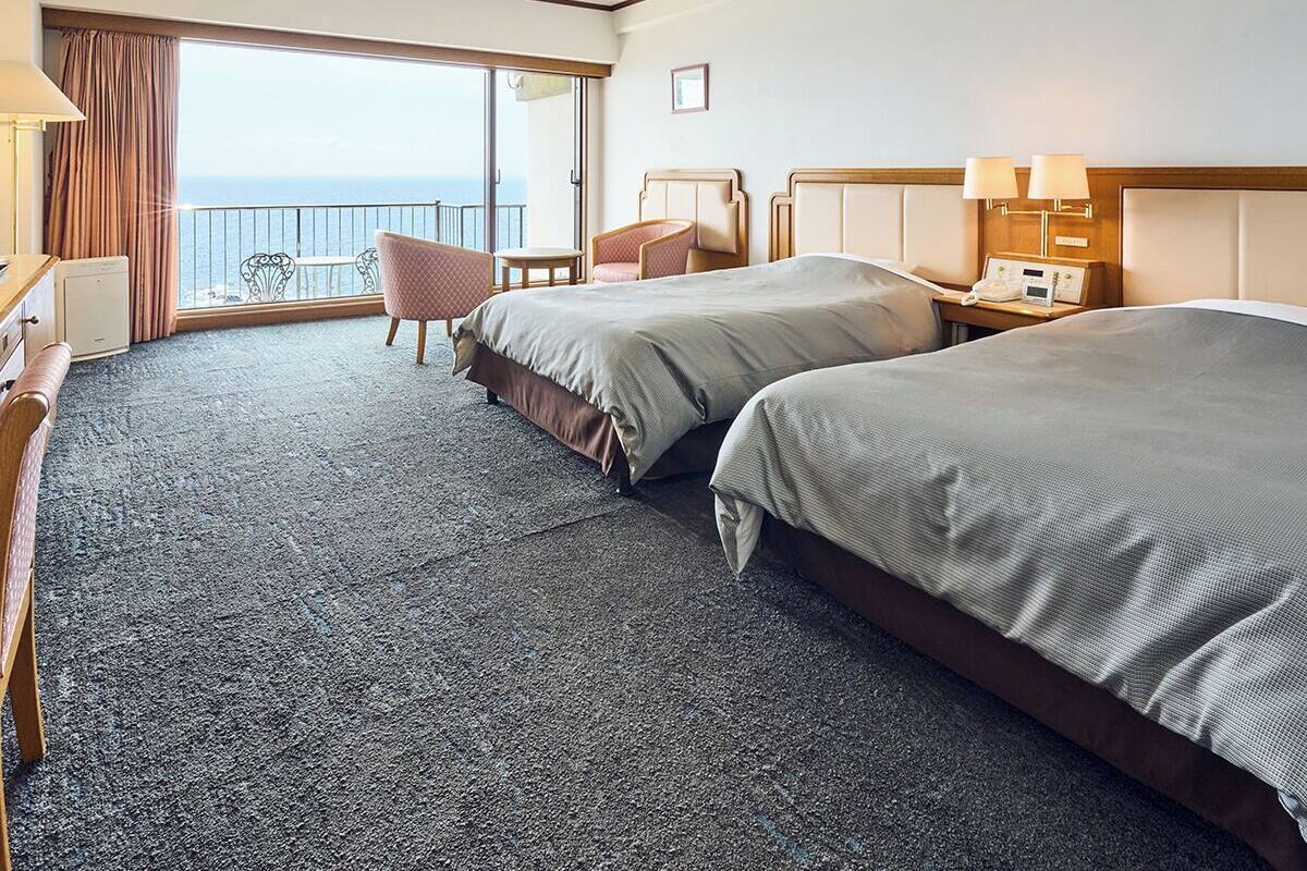 Une chambre d’hôtel avec deux lits, un bureau, une chaise et un balcon donnant sur la mer.
