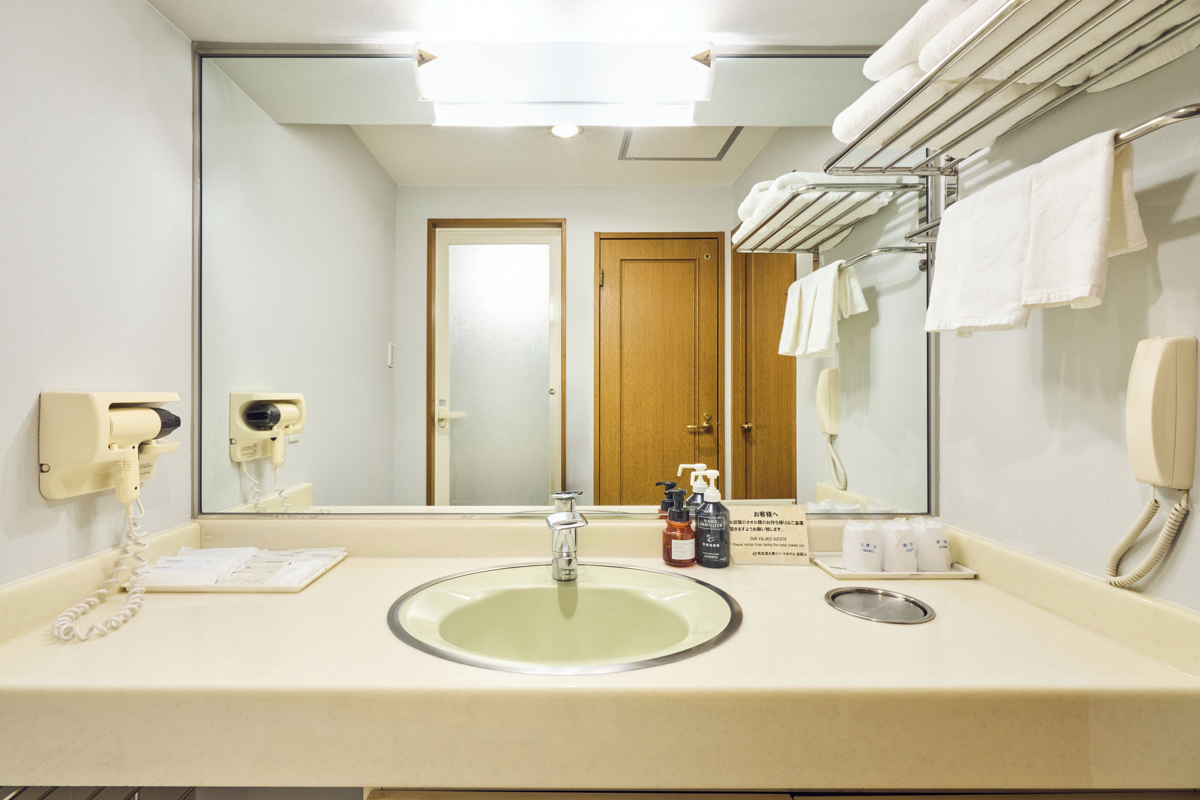 A hotel bathroom with a sink, mirror, towel rack, and a phone.